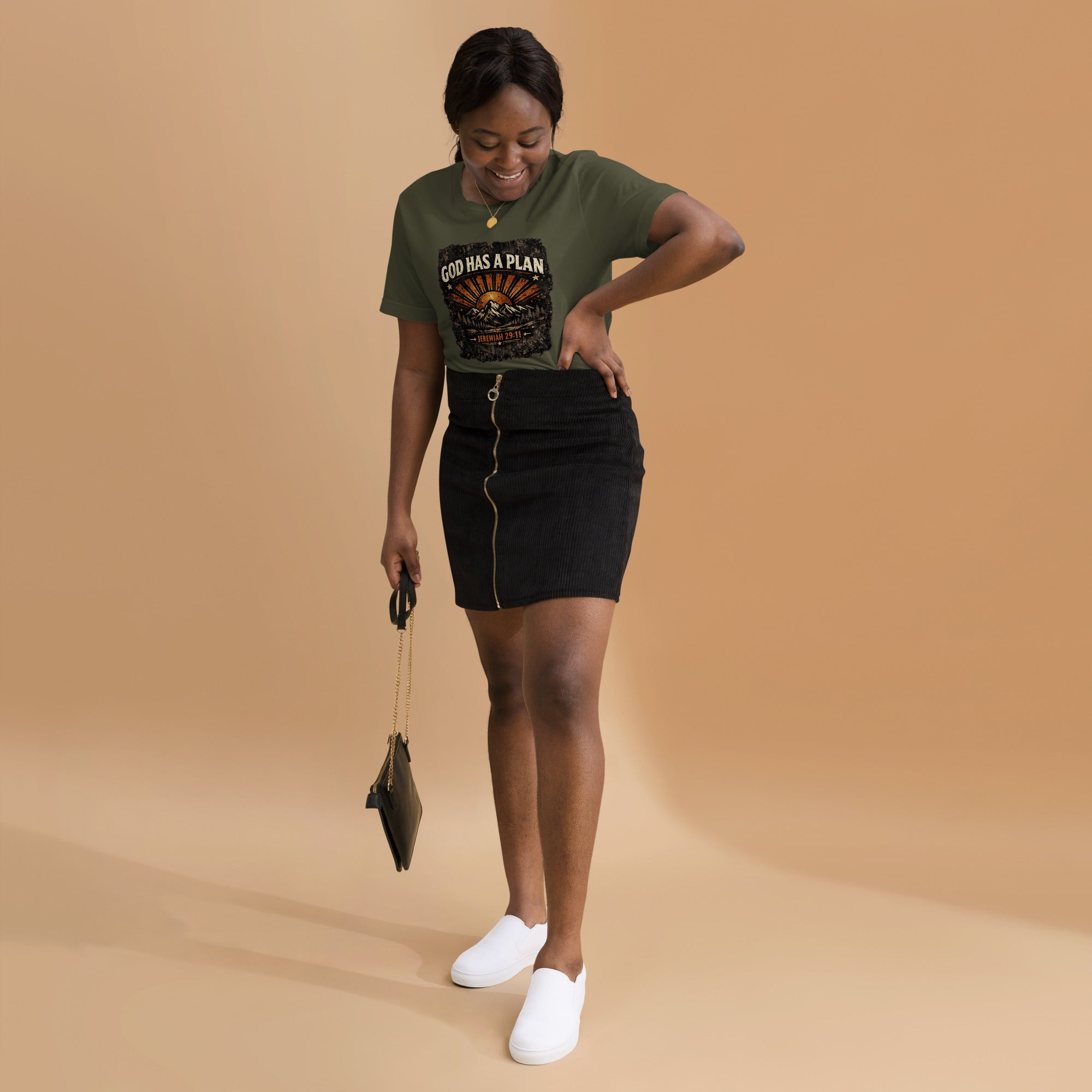 Woman wearing a green t-shirt with 'God Has A Plan' text, black skirt, and white shoes on a beige background