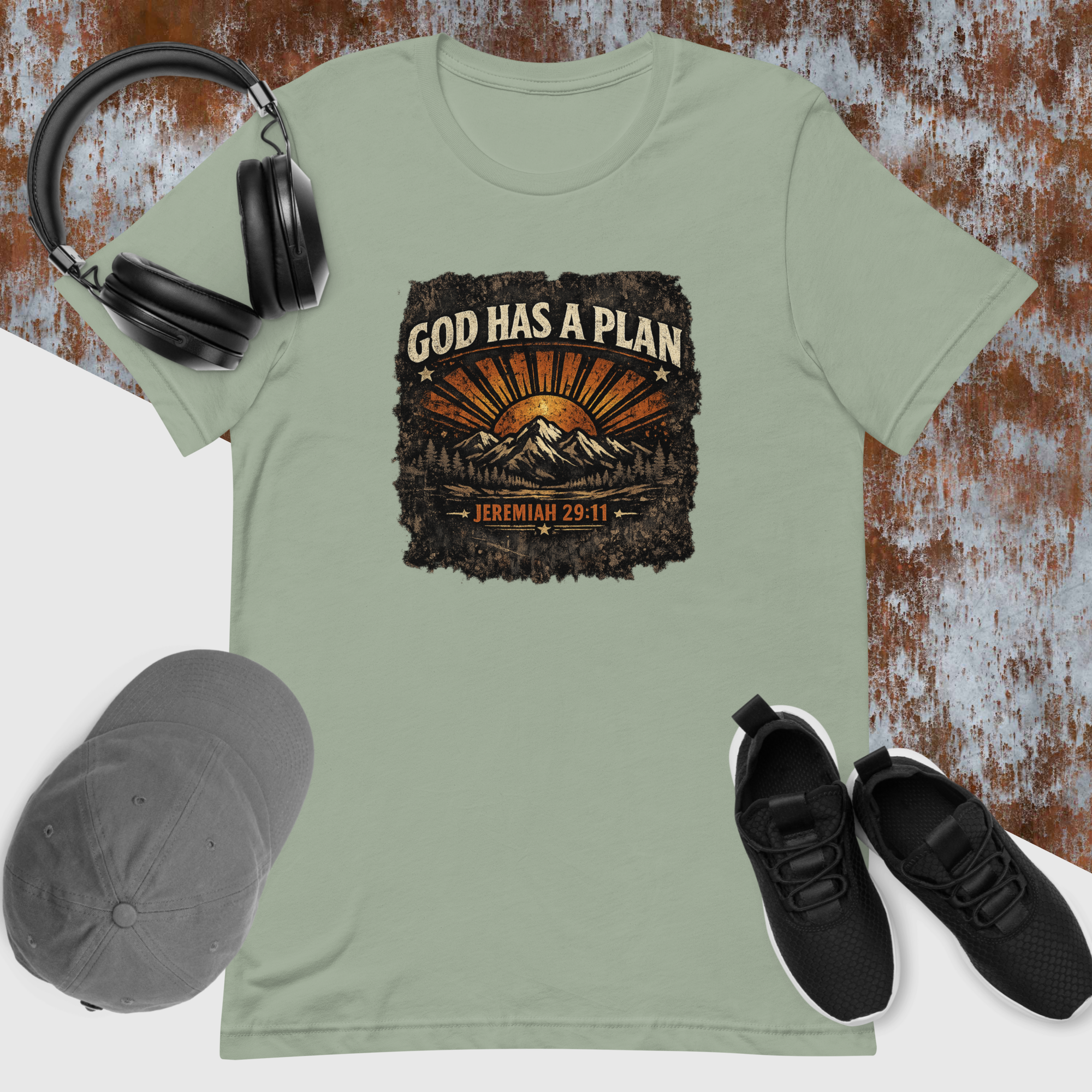 Green t-shirt with 'God Has a Plan' graphic, black sneakers, cap, and headphones on a textured surface.