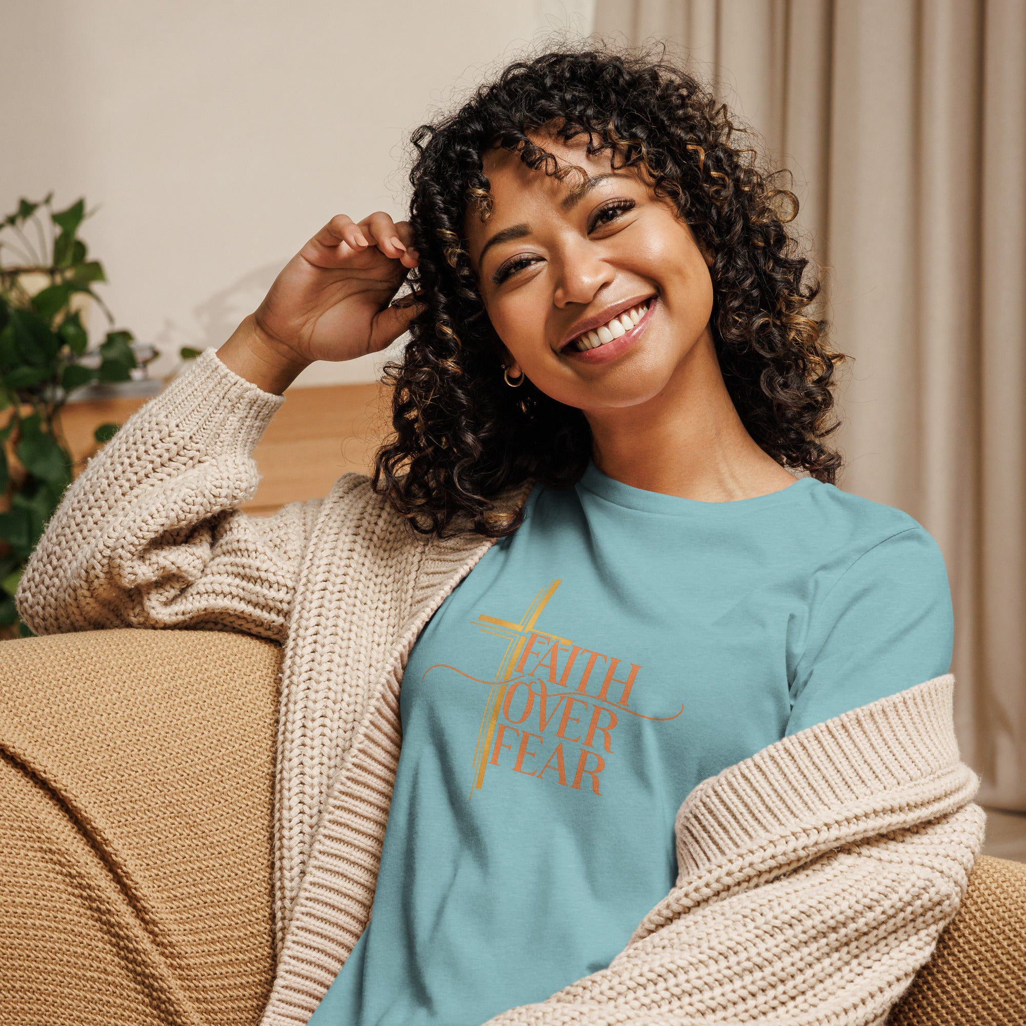 Woman wearing a blue sweatshirt with 'Faith Over Fear' text, sitting on a couch.