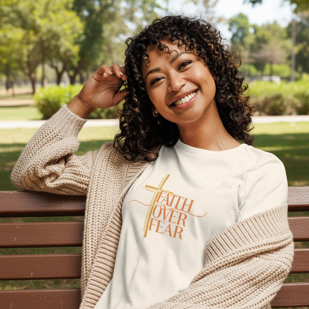 Woman wearing a white t-shirt with pink text Faith Over Fear, sitting on a couch.
