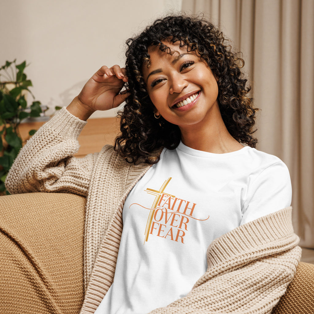 Woman wearing a white t-shirt with Faith Over Fear pink text, sitting on a couch.