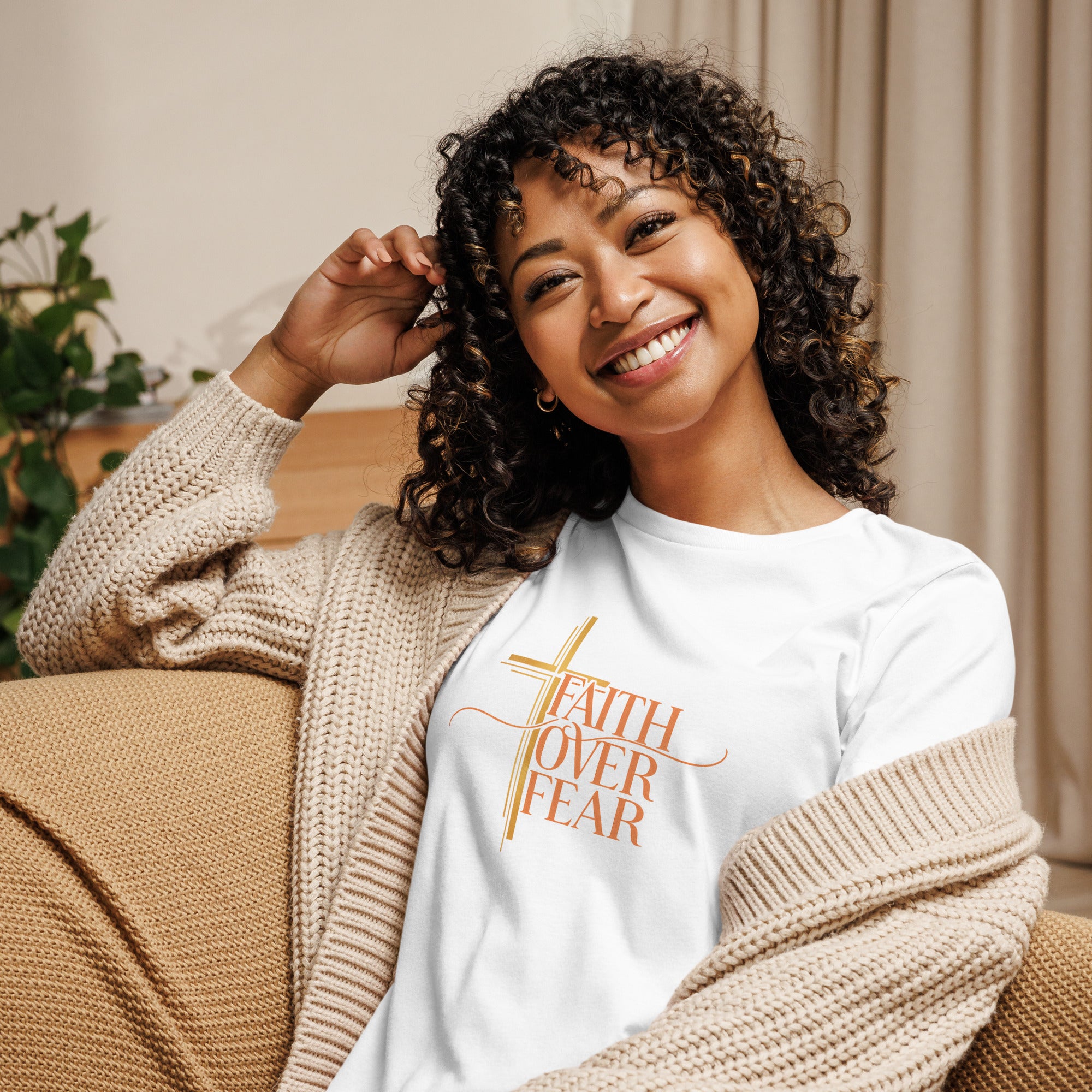 Woman wearing a white t-shirt with Faith Over Fear pink text, sitting on a couch.